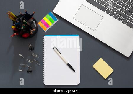 Workplace in the office. Gray table. The photo shows a laptop, colorful stickers, pencils, office accessories. Multicolored pencils lie near the noteb Stock Photo