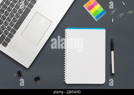 Workplace in the office. Gray table. The photo shows a laptop, colorful stickers, pencils, office accessories. Multicolored pencils lie near the noteb Stock Photo