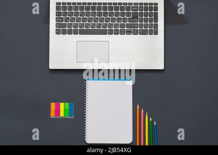 Workplace in the office. Gray table. The photo shows a laptop, colorful stickers, pencils, office accessories. Multicolored pencils lie near the noteb Stock Photo