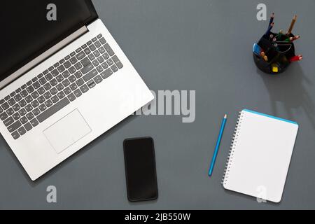 Workplace in the office. Gray table. The photo shows a laptop, colorful stickers, pencils, office accessories. Multicolored pencils lie near the noteb Stock Photo