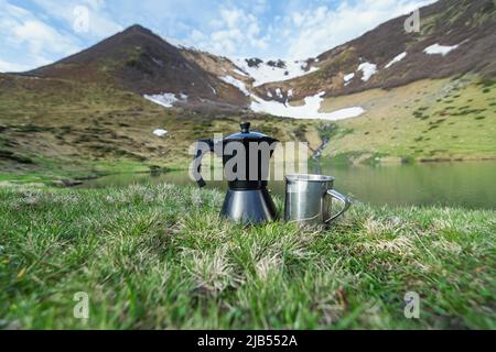 Coffee from a geyser coffee maker is poured into a cup, breakfast on a high-altitude lake in the Carpathians, in the background Lake Vorozheska with b Stock Photo