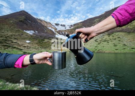 Coffee from a geyser coffee maker is poured into a cup, breakfast on a high-altitude lake in the Carpathians, in the background Lake Vorozheska with b Stock Photo