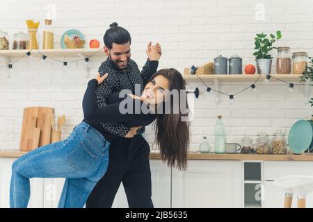 Funny happy good-looking young couple smiling and dancing in their new bright kitchen. High quality photo Stock Photo