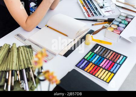 Female artist creating picture at workplace using gouache, watercolor paints set and paintbrush collection. Inspired having idea of new image in the w Stock Photo