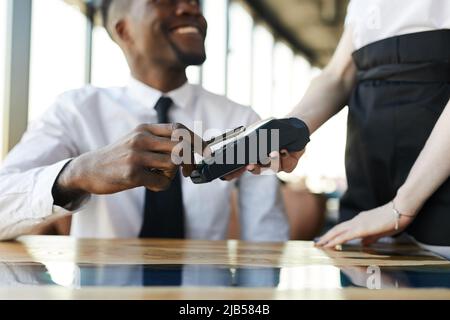 Close-up of smiling black businessman sitting at table and using nfc technology for mobile payment in restaurant Stock Photo