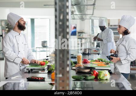 Diverse food industry workers discussing about gourmet dish recipe while cooking in professional kitchen. Chefs talking about what meal to prepare for dinner service at fine dining restaurant. Stock Photo