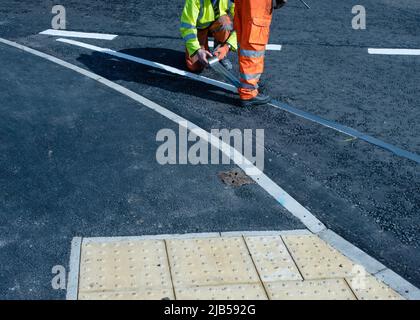 Roadworker applying thermoplastic road marking on the freshly laid tarmac during new roundabout and road construction Stock Photo