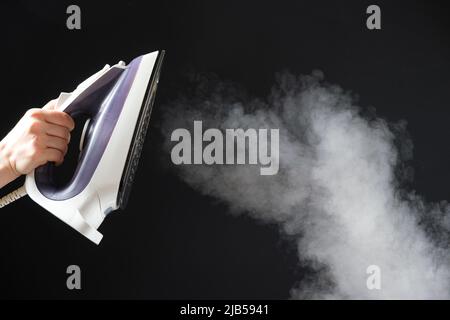 An iron with a steam generator sprays white hot steam on a black background. Steaming clothes, ironing. Stock Photo