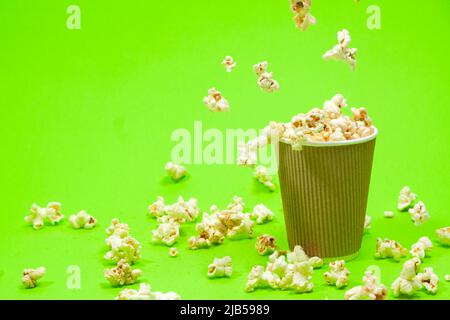 Popcorn is poured into a paper brown glass on a green background with place for text. Stock Photo