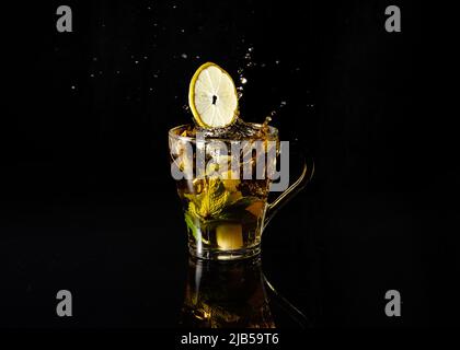 splash in a cup of tea with mint and lemons on black background Stock Photo
