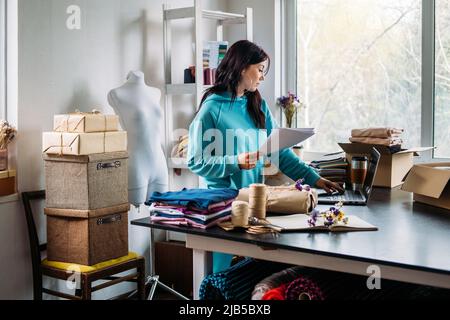 Young woman tailor fashion designer dressmaker using laptop in seamstress studio Stock Photo