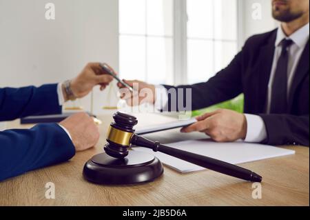 Wooden brown gavel of judge against background of lawyer and client signing legal contract. Stock Photo