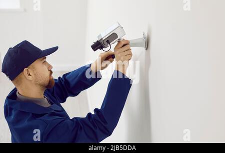 Professional male technician repairs or installing cctv camera system on wall inside house. Stock Photo