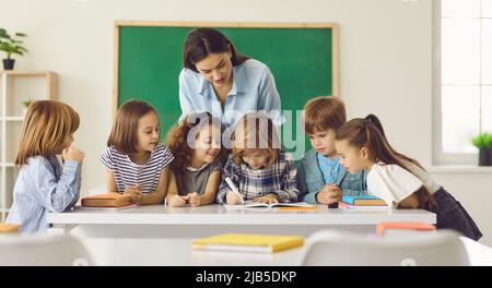 Teacher and children looking at classmate doing homework writing on copybook Stock Photo