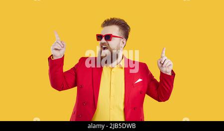 Cheerful and stylish young extravagant chubby man having fun and dancing on yellow background. Stock Photo