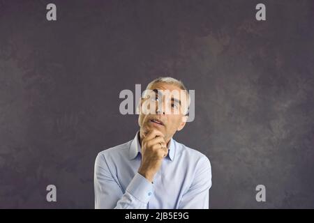 Studio headshot portrait of senior questionable man who is looking up thinking or planning. Stock Photo