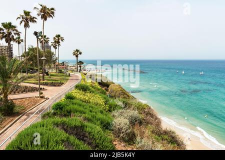 the promenade and resort hotels on a cliff high above the Mediterranean beach at Netanya in Israel with a couple walking, sail boats and kitesurfing Stock Photo