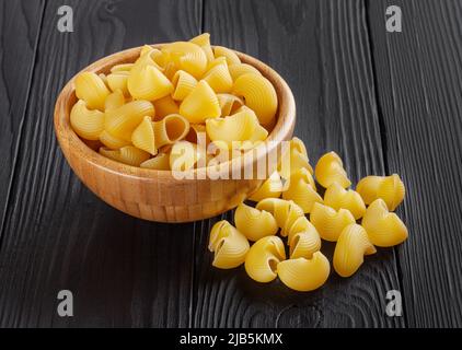 Uncooked pipe rigate pasta in wooden bowl on black wooden background Stock Photo