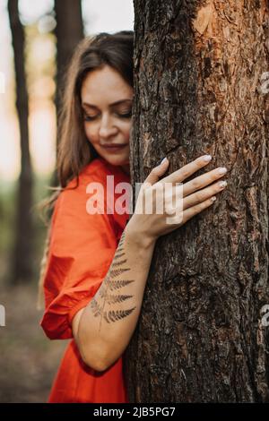 Woman with fern tattoo hugging trees and enjoying nature in the pine forest. Stock Photo