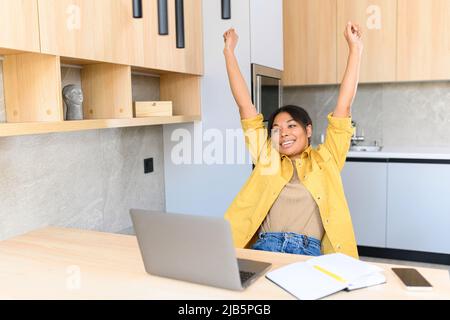 Cheerful female office employee stretching arms sitting at office desk, woman is preparing for productive work with laptop or resting after finished project, takes break and doing exercises for back Stock Photo