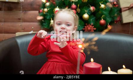 A little girl with a pencil in her hand looks at a lit firework sparkler. Stock Photo