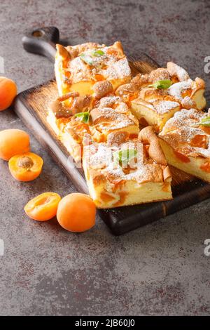 Slices of fresh apricot iced sponge cake with fruits closeup on the wooden board on the table. Vertical Stock Photo