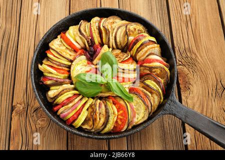 Tasty vegetarian ratatouille made of eggplants, squash, tomatoes and onions in black cast iron pan on wooden table horizontal Stock Photo