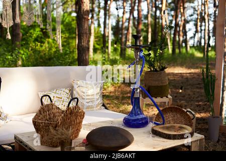 Lounge zone with hookah, diy sofa and table of cargo pallets in boho style on outdoor wedding ceremony venue in pine forest. Bohemian decor. Stock Photo