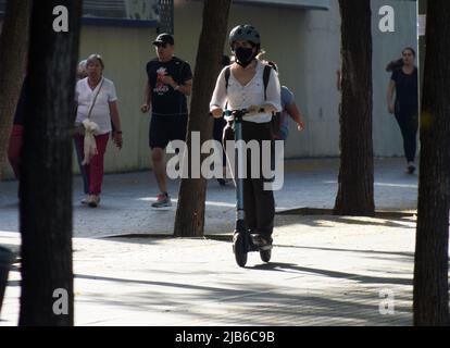 Woman with helmet and mask riding on an electric scooter in a street. Stock Photo