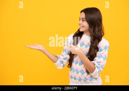 Look at advert. Teenager child points aside shows blank copy space for text promo idea presentation, poses against yellow background. Stock Photo