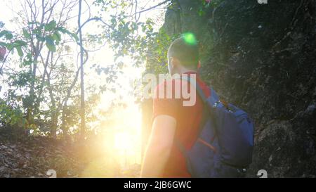 Free hiker with backpack on mountain edge looking at sun and enjoy beautiful sunset. Happy traveler man in rays of sunrise. Man dream concept. Sun Stock Photo