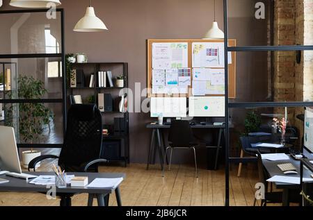 Image of modern office with workplaces of employees with computers on them and board with documents hanging on wall Stock Photo
