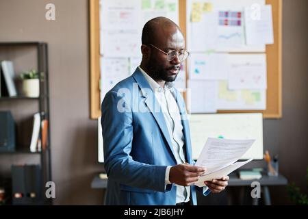 African businessman in eyeglasses examining business documents while standing at office Stock Photo