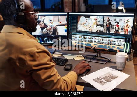 African colorist in headphones looking at project on table and checking the work on computer monitor at table Stock Photo