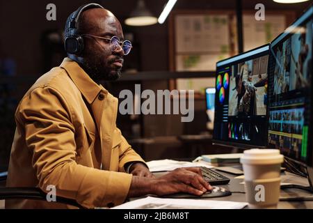 Serious African colorist in eyeglasses concentrating on his work at table, he making photo editing on computer Stock Photo