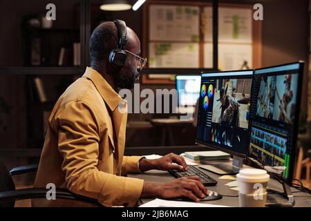 African male colorist in headphones and eyeglasses working on photo design with multimedia software on computer at office Stock Photo