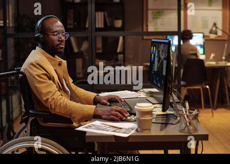 African man in wheelchair editing a video using post production software wearing headphones Stock Photo