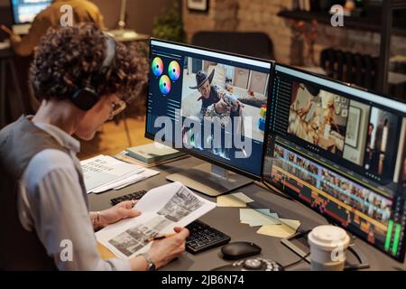 Young female editor examining script while working at table on computer with big display Stock Photo