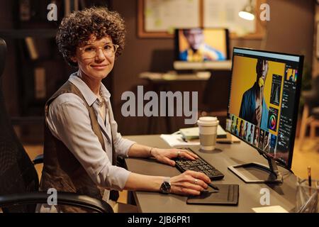 Portrait of young female designer smiling at camera while using tablet pen for editing photos on computer screen at office Stock Photo