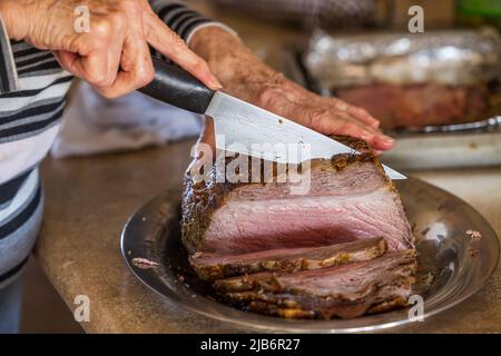 A woman slicing a large prime rib beef roast that was baked and roasted in the oven by a home gourmet chef for a holiday Christmas dinner Stock Photo