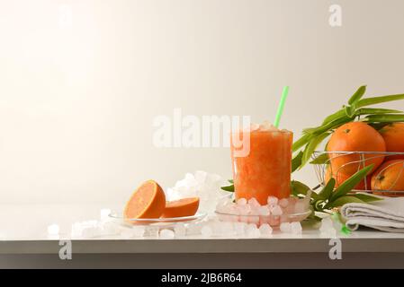 Detail of orange drink with a lot of ice on a white table with fruit and a bowl with ice around it and isolated background. Front view. Horizontal com Stock Photo