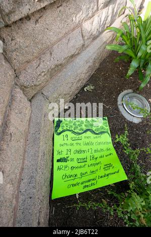 Austin Texas USA, May 30 2022: A protest sign lies near the Texas Capitol memorials honoring the 21 victims of the Uvalde, Texas school massacre on May 24. The handwritten sign reads '19 armed men were outside the Uvalde classroom yet 19 children and 2 adults die by an armed 18 year old with AR 15 assault weapon. Change gun laws! Create universal background checks!' Stock Photo