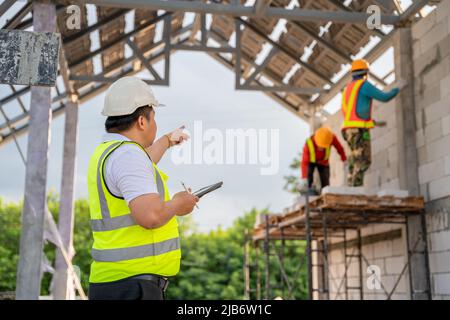Asian Civil Engineers are working with construction workers who are laying bricks at the construction site. Stock Photo