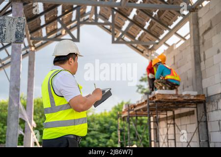 A civil engineer is supervising a construction worker laying bricks at a construction site. Stock Photo