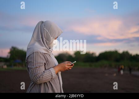 Makassar, South Sulawesi, Indonesia. 3rd June, 2022. A woman holding a cellphone while enjoying the atmosphere on the edge of Bosowa Beach, Makassar. This beach gets crowded on weekends by tourists to enjoy the beach view and sunset (Credit Image: © Herwin Bahar/ZUMA Press Wire) Stock Photo