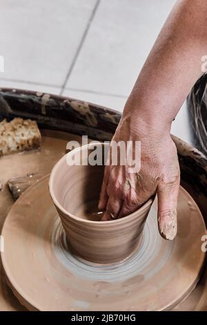 Hand of senior woman sculpting clay vase on potter's wheel. Stock Photo