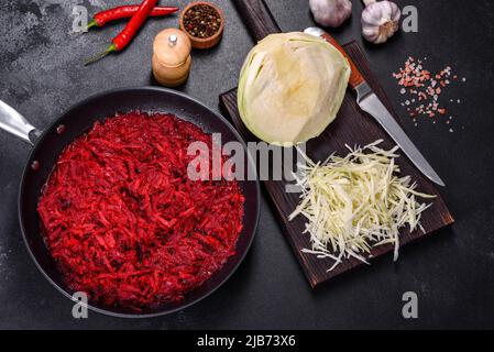 Chopped beetroot in a pan as well as spices and herbs on a wooden cutting board as ingredients in the preparation of traditional Ukrainian borscht Stock Photo