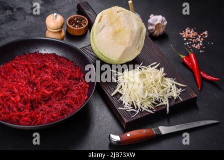 Chopped beetroot in a pan as well as spices and herbs on a wooden cutting board as ingredients in the preparation of traditional Ukrainian borscht Stock Photo