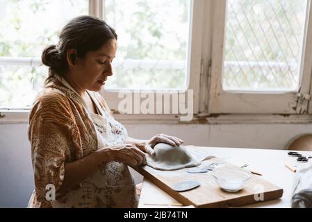 Young woman working clay and ceramic at home, making handmade pottery and bowls. Concept of craftsmanship and creativity at home. Stock Photo