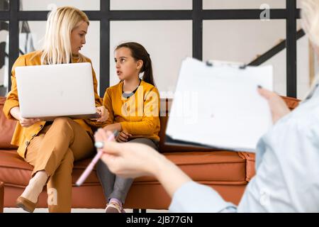 Rear view of female psychologist helping young family with a kid to solve child development problems. Family sitting on a sofa Stock Photo